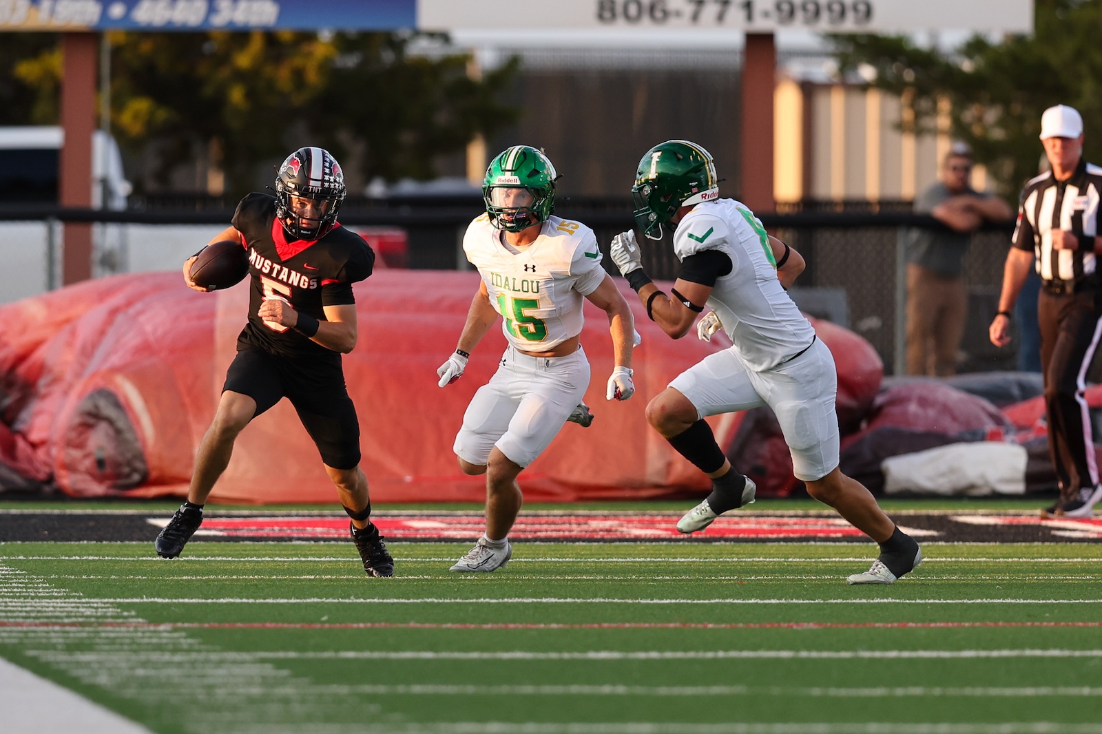 Seabolt Chase-16748 | Press Pass Sports A football player in a black Mustang jersey runs with the ball while being chased by two white-uniformed defenders on a green turf field.
