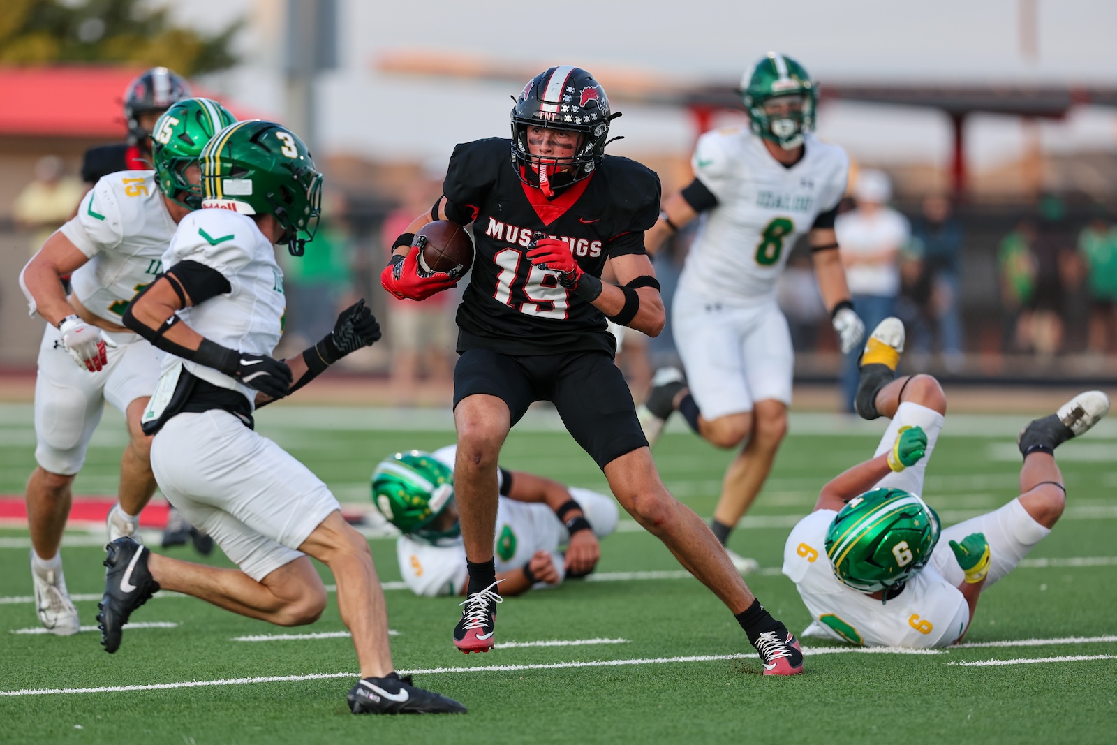 Seabolt Chase-17010 | Press Pass Sports Football player in black Mustangs uniform runs with the ball while defenders in white/green reach in a crowded field.