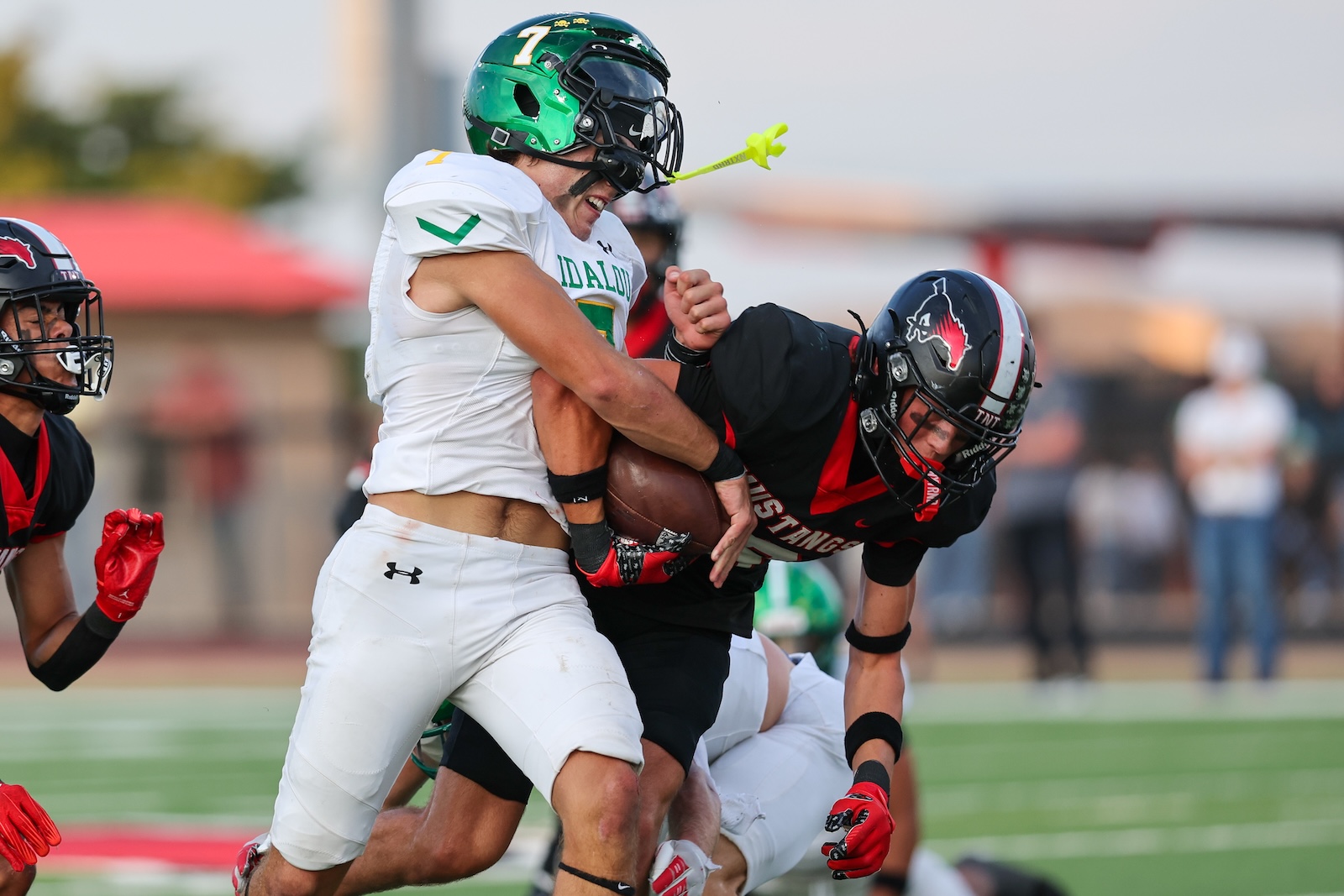 Seabolt Chase-17042 | Press Pass Sports Two football players collide on the field: a ball carrier in a white jersey is tackle‑driven by a defender in black and red.