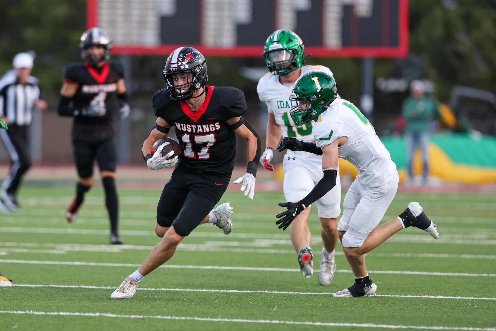 Seabolt Chase-17254 | Press Pass Sports Mustangs running back (#17) carries the ball, chased by defenders on a green football field during a game.