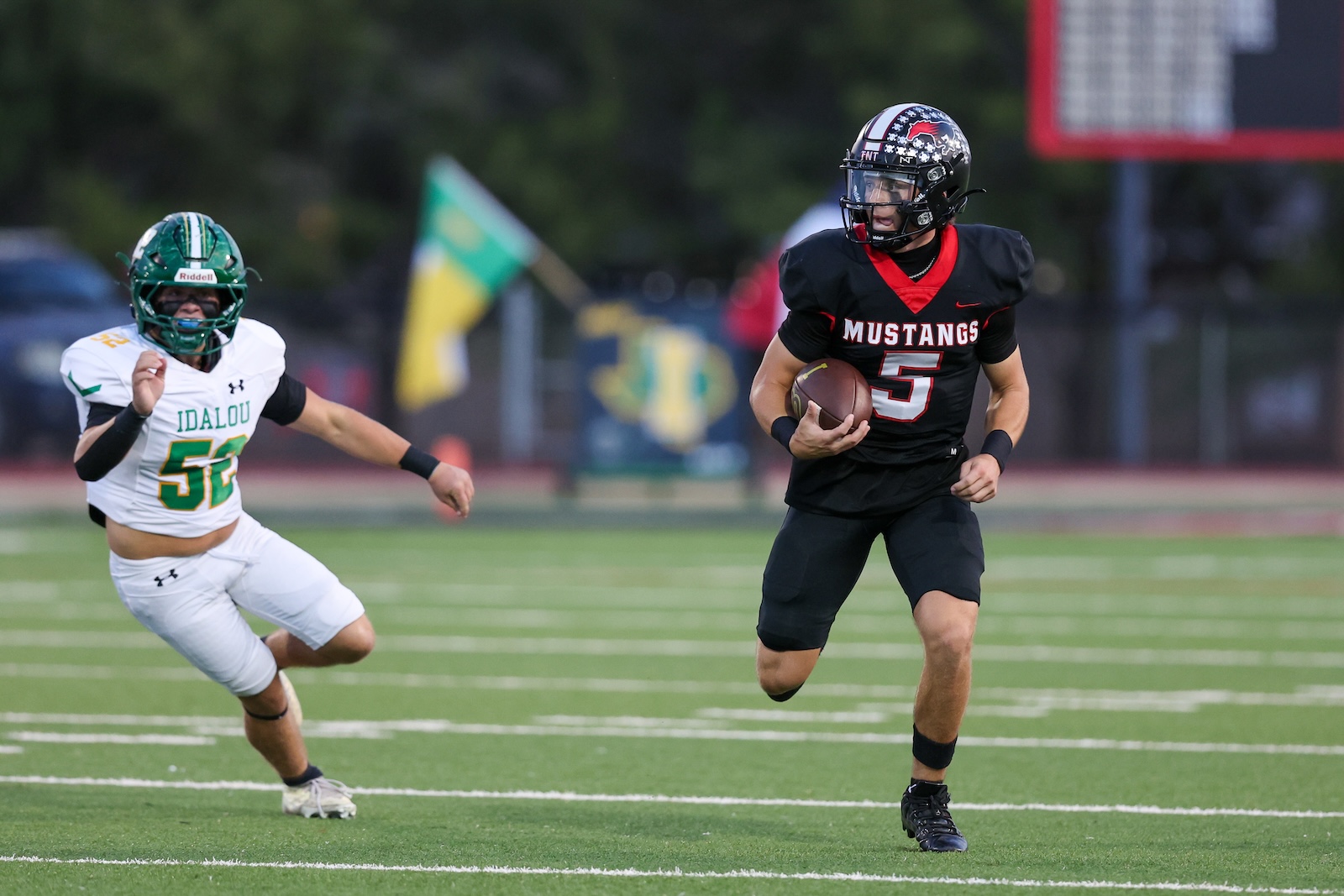 Seabolt Chase-17543 | Press Pass Sports Football game: Mustang #5 carries the ball while Idalou defender #53 in white pursues on a green field.