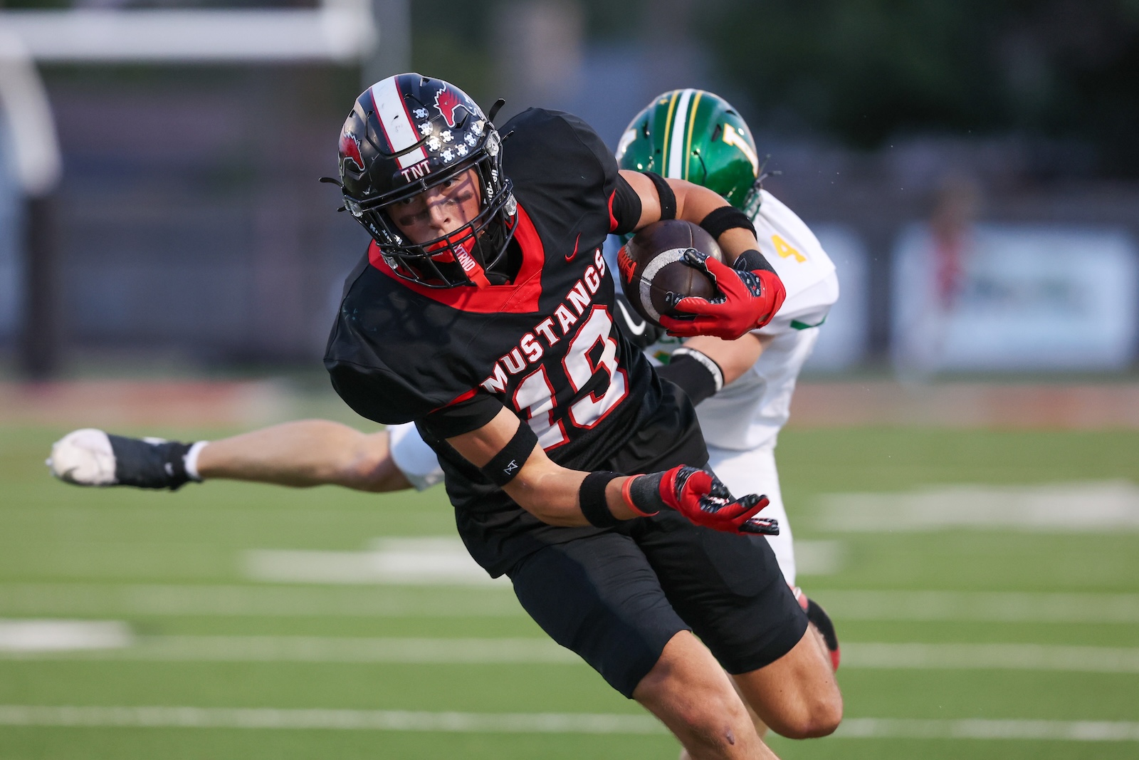 Seabolt Chase-17609 | Press Pass Sports Football player in black Mustangs uniform running with ball while being tackled on a green field.