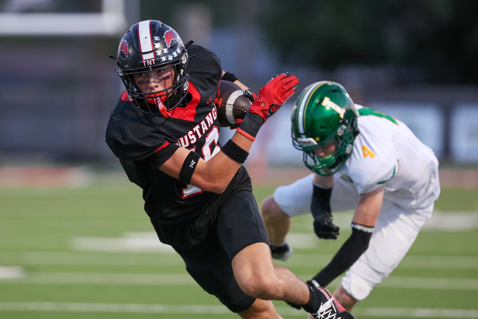 Seabolt Chase-17612 | Press Pass Sports Football player in black Mustang jersey (number 2) breaks a tackle while holding the ball, as a defender in white/green closes in.