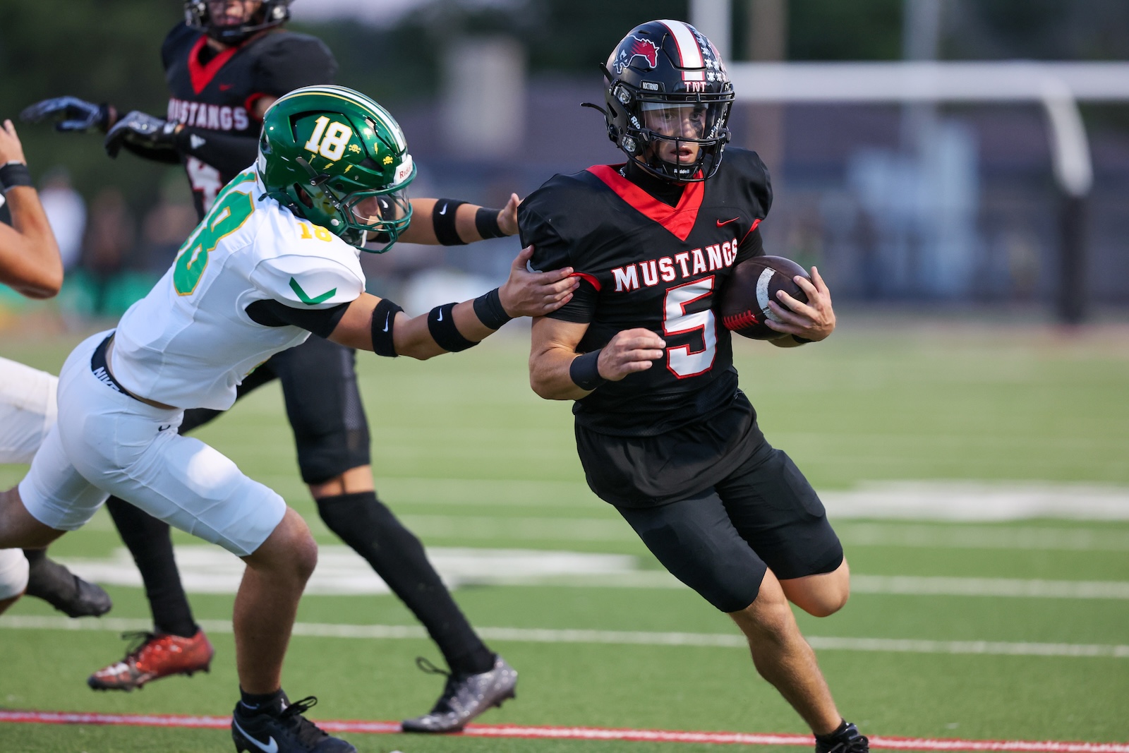 Seabolt Chase-17717 | Press Pass Sports High-school football player in black Mustang uniform with the ball dodges a tackle from a white-and-green defender.