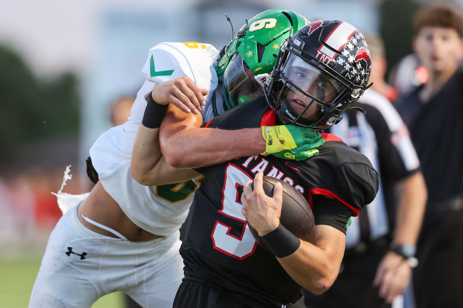Seabolt Chase-17746 | Press Pass Sports Football player in black and red runs with the ball as a defender in white and green tackles him.