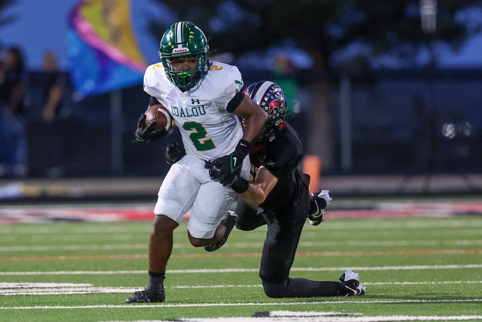 Seabolt Chase-17923 | Press Pass Sports Football player in white Jersey #2 dodges a tackle while holding the ball on a turf field at night.