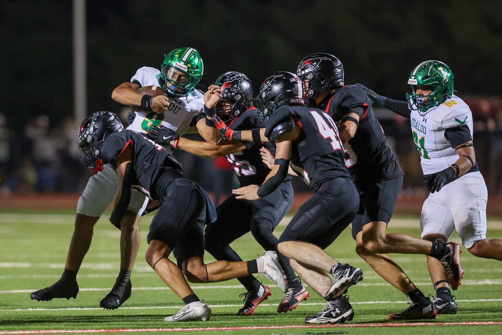 Seabolt Chase-18158 | Press Pass Sports Group of football players collide at the line of scrimmage during a nighttime game on a green field with white markings.