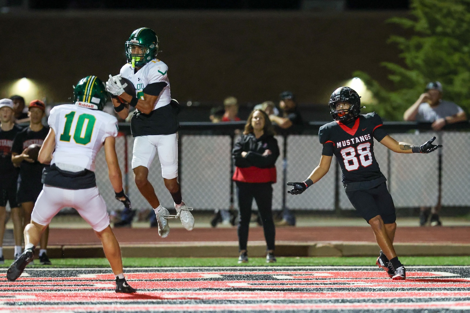 Seabolt Chase-18687 | Press Pass Sports Football players in a night game: a white-uniform receiver leaps to catch a pass as a teammate (#10) moves in, while a Mustang (#86) guards on the right.