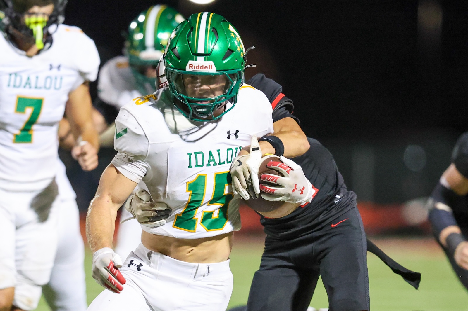Seabolt Chase-18822 | Press Pass Sports Idalou football player number 15 carrying the ball, tackled by a defender during a night game.