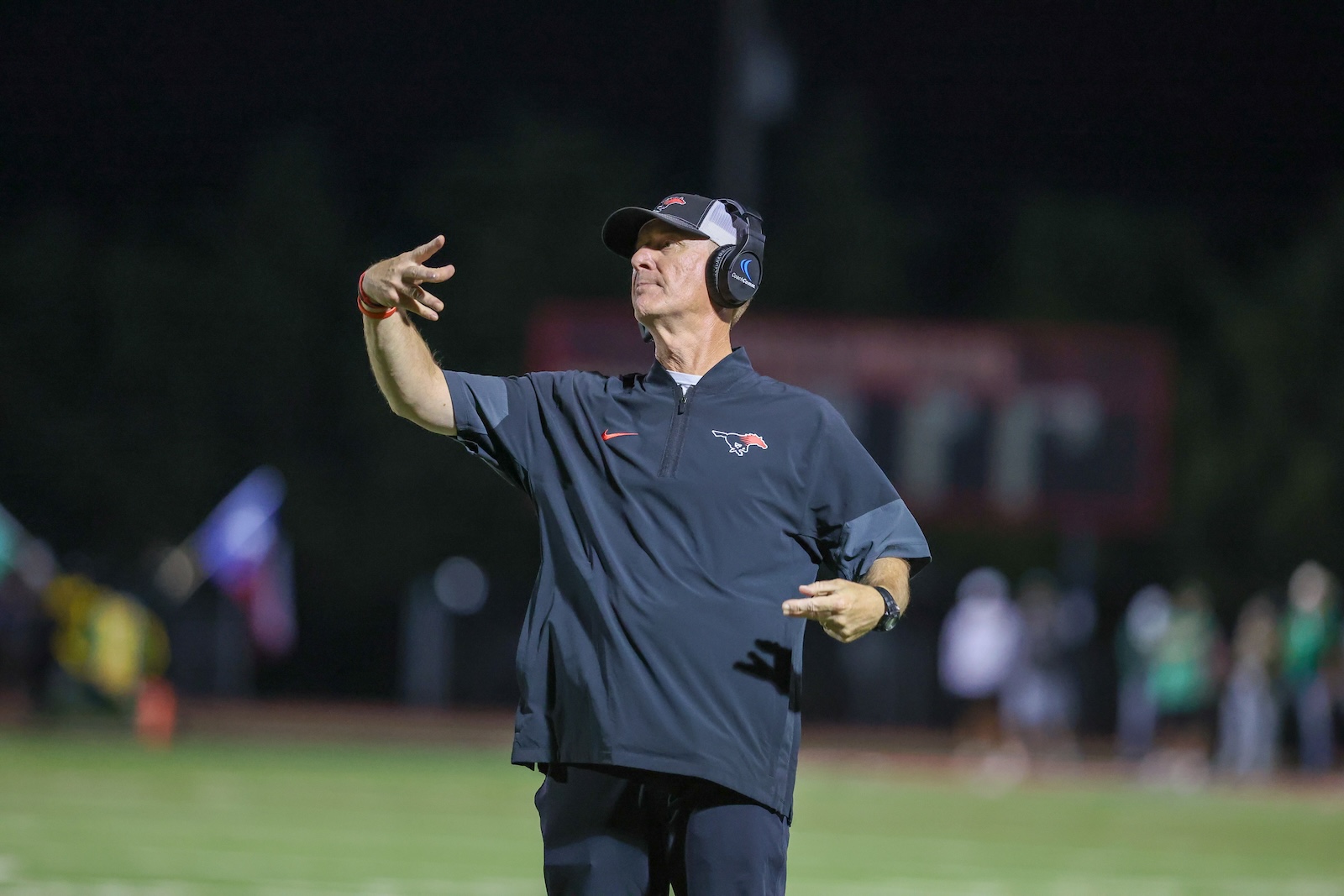 Seabolt Chase-19251 | Press Pass Sports Football coach on a night field signaling a play, wearing a cap and headset.