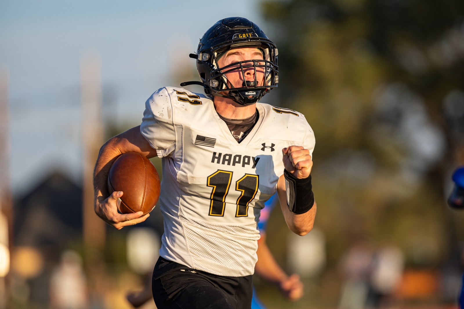 Liberty_15-11 | Press Pass Sports Football player in a white jersey with number 11 runs with the ball, helmet on, during a game.