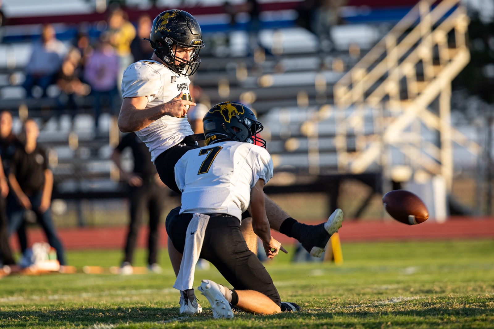Liberty_15-13 | Press Pass Sports Two football players in white jerseys collide on a grassy field as a ball sails toward the ground.