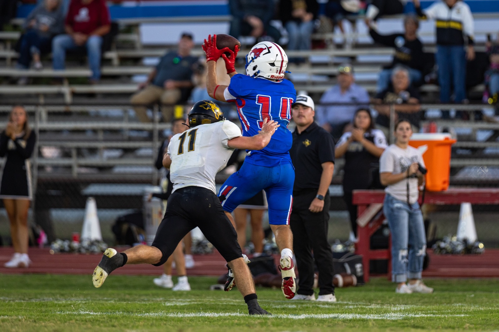 Liberty_15-25 | Press Pass Sports Blue-jersey football player leaps to catch the ball while a defender in white reaches in from the side, midair action on the field.