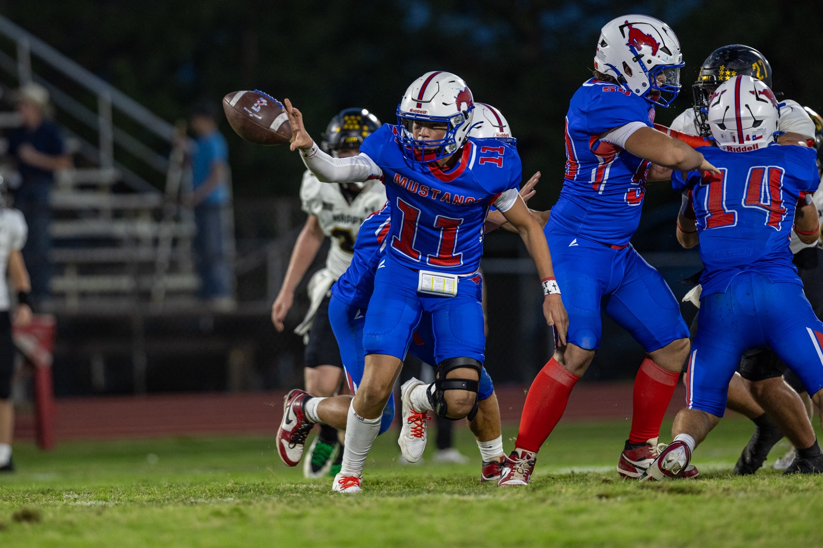 Liberty_15-35 | Press Pass Sports QB in blue #11 throws a football as teammates block during a nighttime football game.