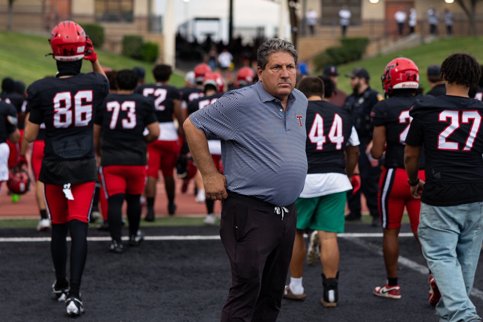 007A5592 | Press Pass Sports Coach with hands on hips stands among a football team on a track after a game.
