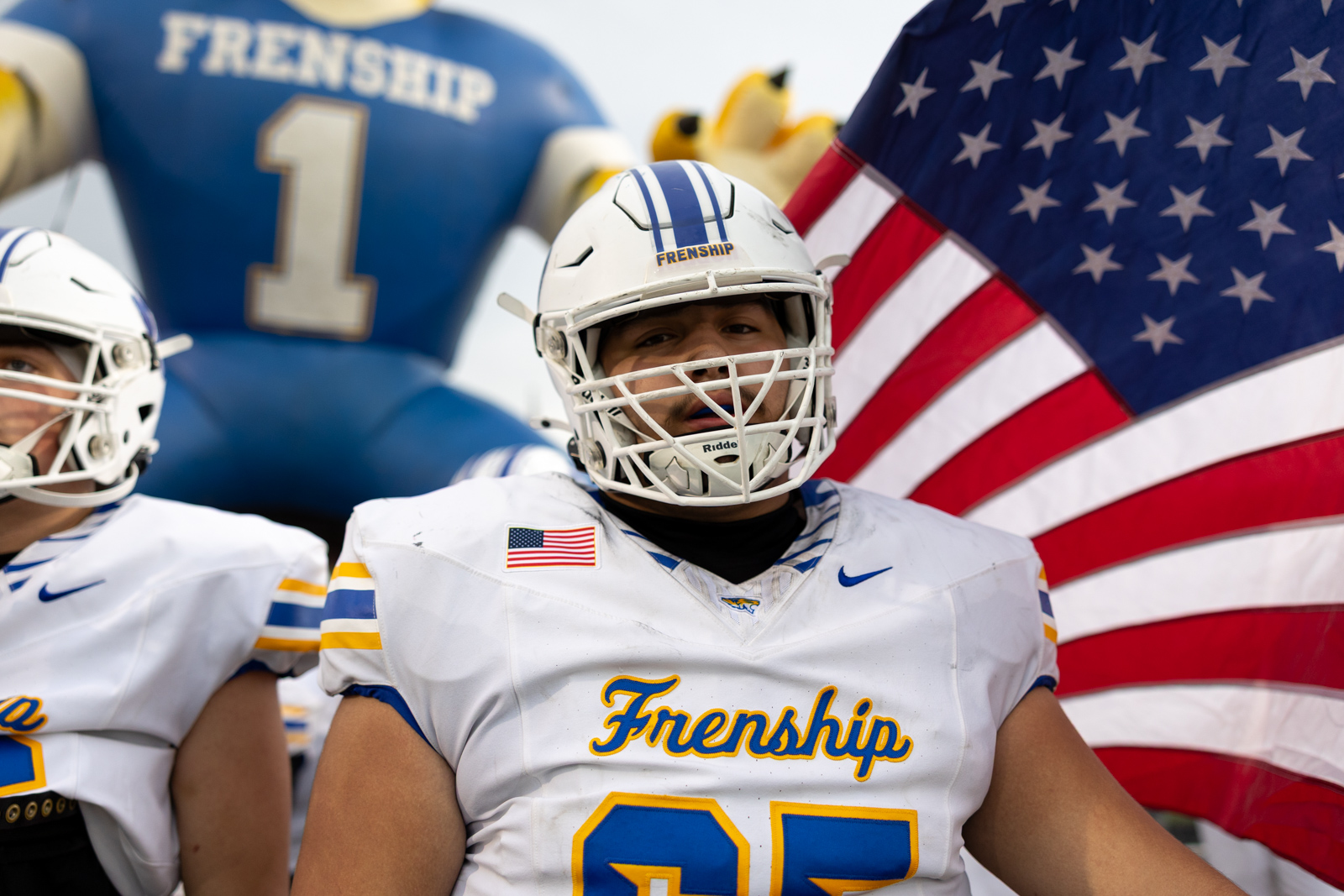 007A5635 | Press Pass Sports American football player in a white Frenship jersey and helmet, with an American flag in the background.