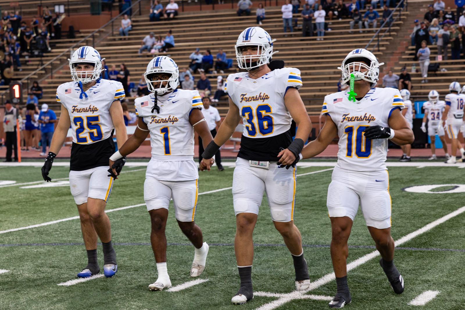 007A5662 | Press Pass Sports Frenship football players in white uniforms walk onto the field before a game, with stands in the background.