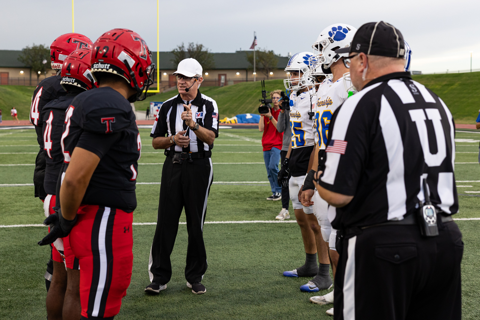 007A5677 | Press Pass Sports Referee conducts a coin toss with two football teams lined up on the field before kickoff at midfield.