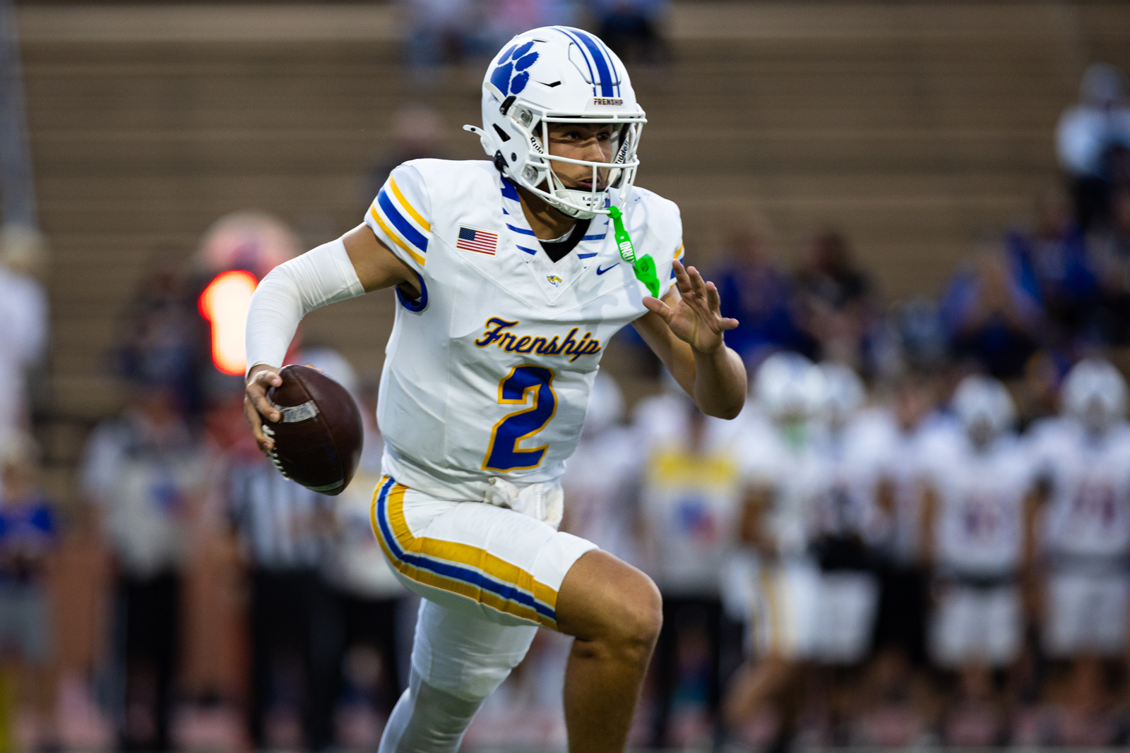 012A5559 | Press Pass Sports Football player in white uniform with blue/yellow stripes running with a ball during a game (helmet with blue paw print)