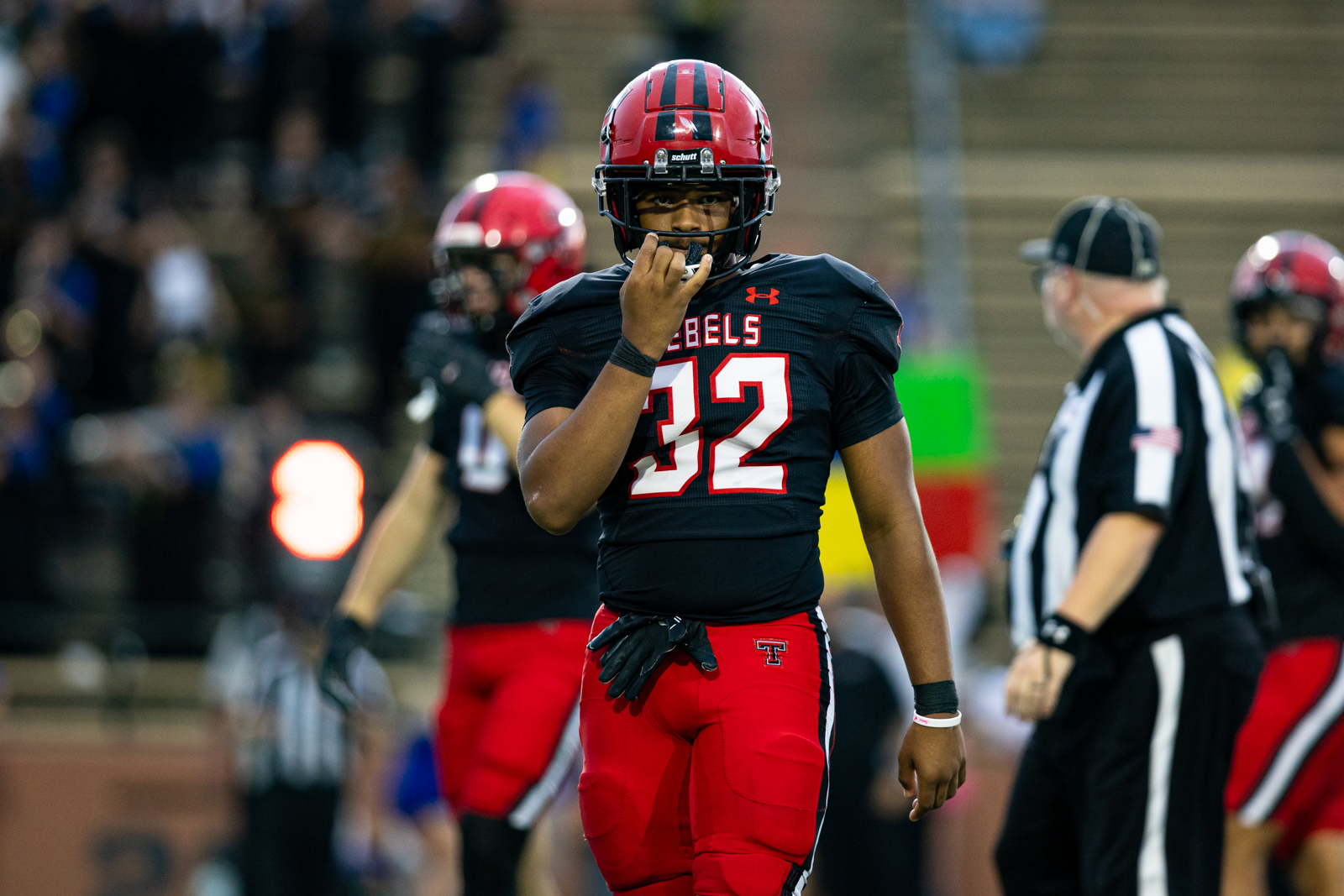 012A5601 | Press Pass Sports Football player in a black and red uniform, number 32, adjusting his mouthguard on the field