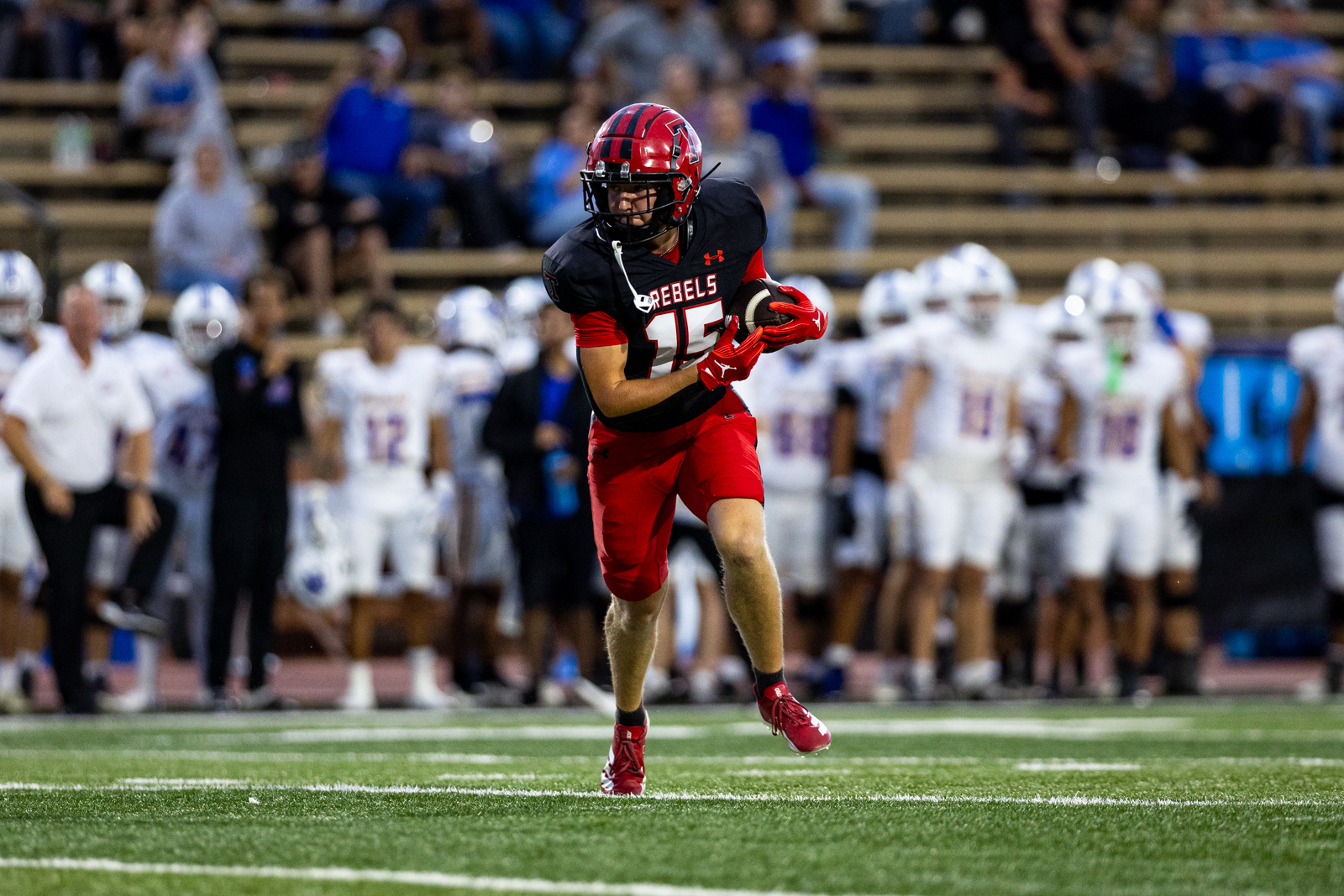 012A5738 | Press Pass Sports Football player in black and red jersey with the number 15, sprinting with the ball during a game on a green turf field.