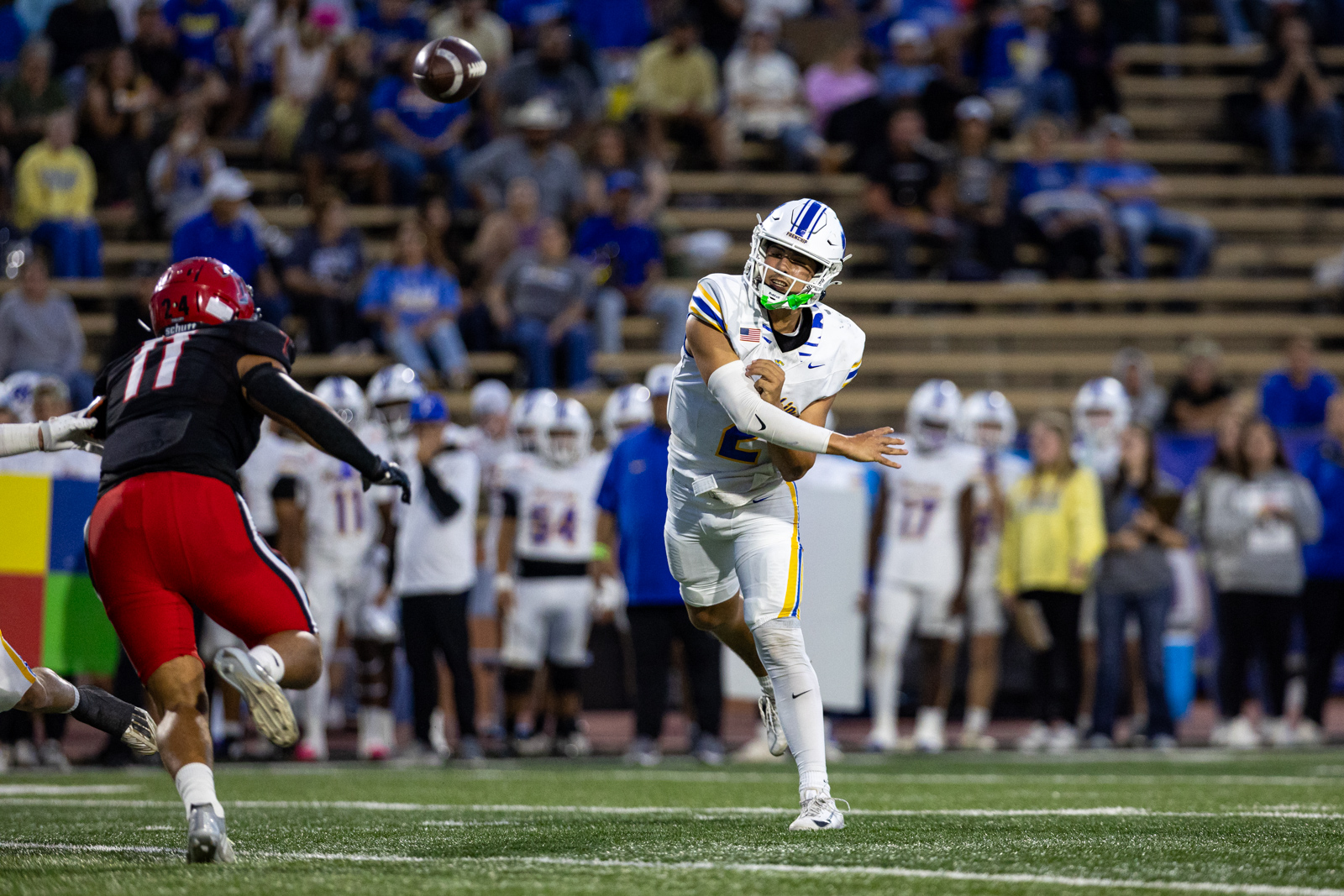 012A5924 | Press Pass Sports Quarterback in white and blue throws a pass as a defender in red closes in on the field.