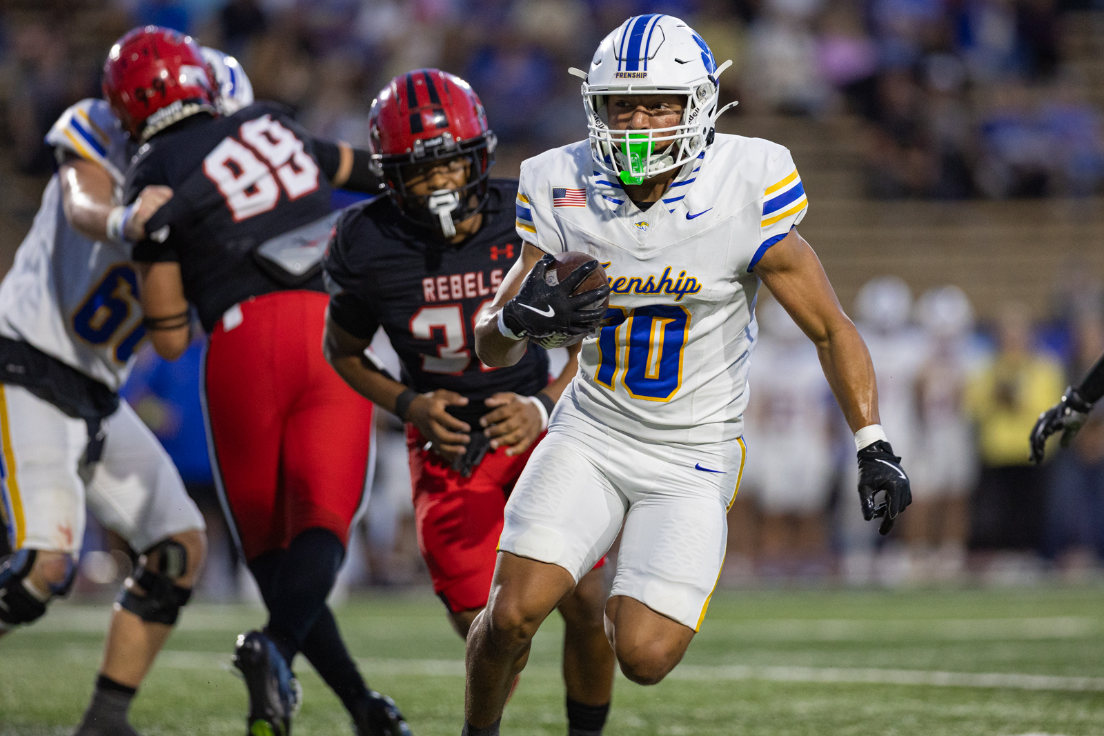 012A5952 | Press Pass Sports White football player (number 10) in a Freneship jersey runs with the ball as defenders in red and black pursue him on a turf field.