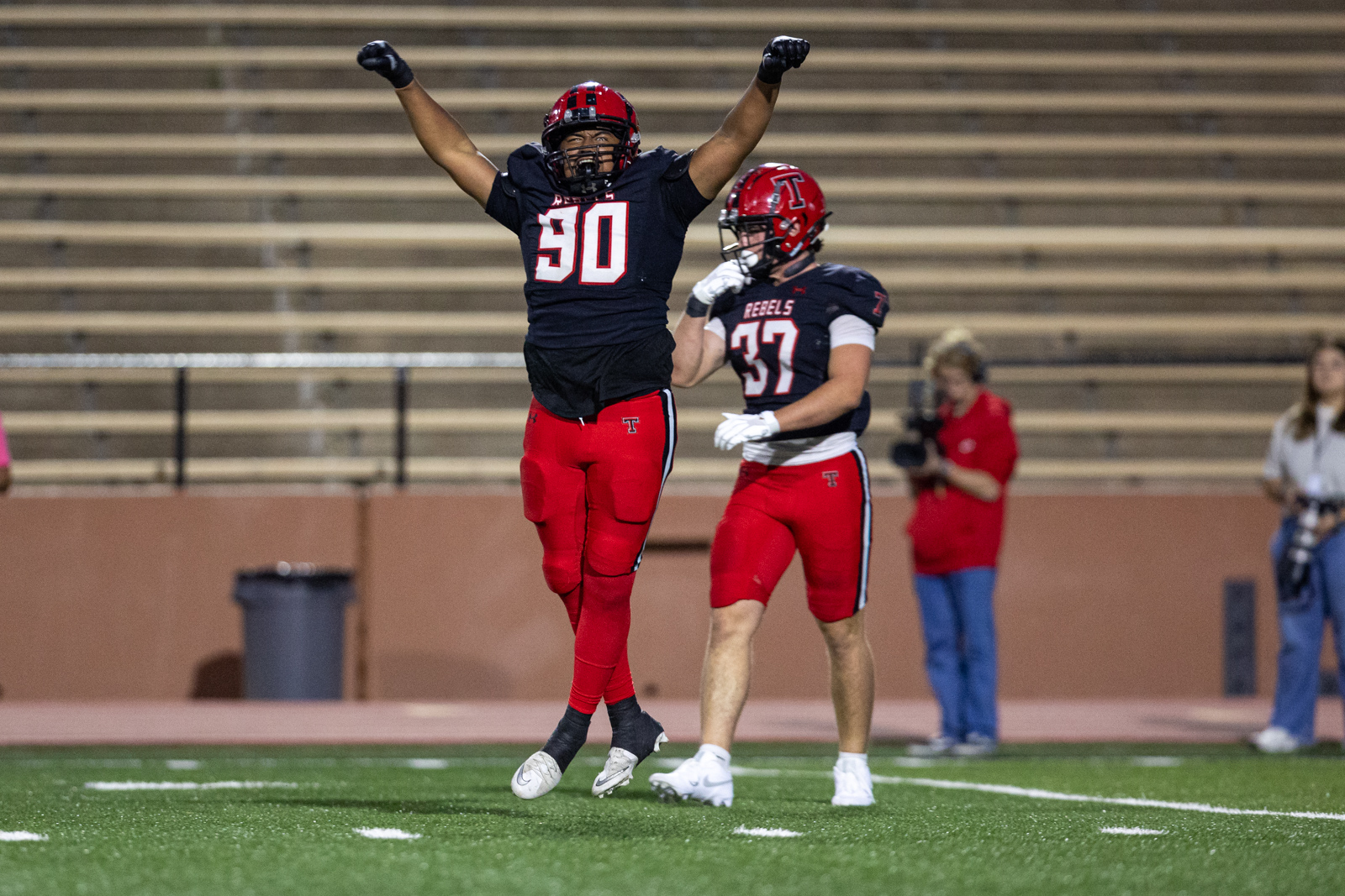 012A6314 | Press Pass Sports Football players from the Rebels celebrate a play on the field; #50 jumps with arms raised as teammate looks on.