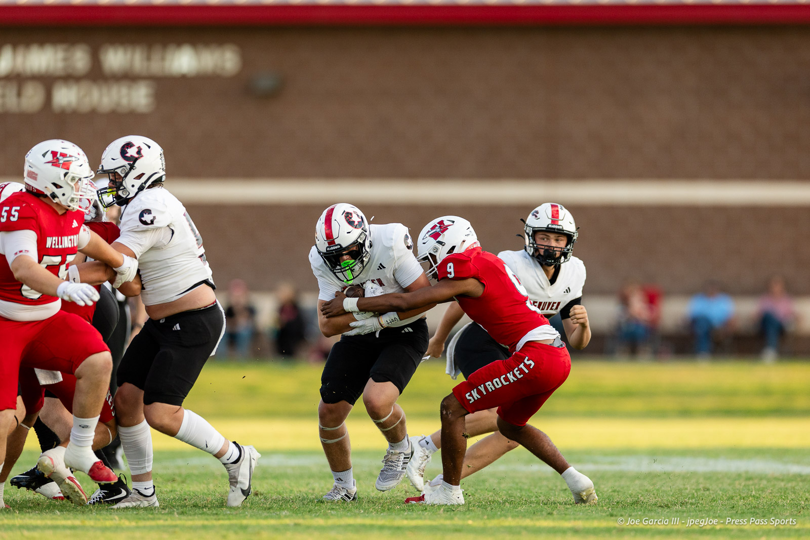 gruver-vs-wellinton-2026-jpegJoe-pps-1 | Press Pass Sports Group of football players in white and red uniforms collide on a grassy field during a play, with a ball carrier in white being tackled by a defender in red.