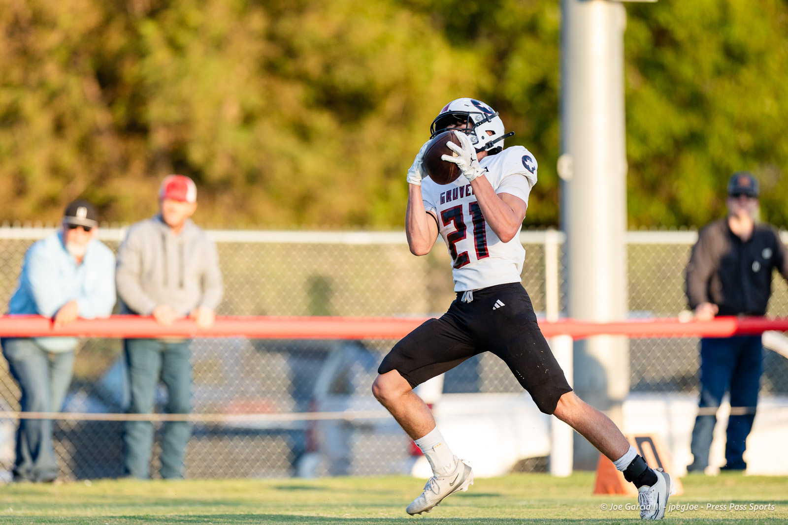 gruver-vs-wellinton-2026-jpegJoe-pps-3 | Press Pass Sports Football player in a white jersey #21 leaps to catch a pass during a game, on a grassy field with spectators in the background.
