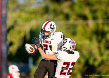 Two Gruver football players in white uniforms leap for the ball; #31 reaches for the catch while #23 defends nearby.