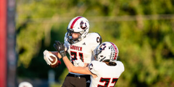 Two Gruver football players in white uniforms leap for the ball; #31 reaches for the catch while #23 defends nearby.