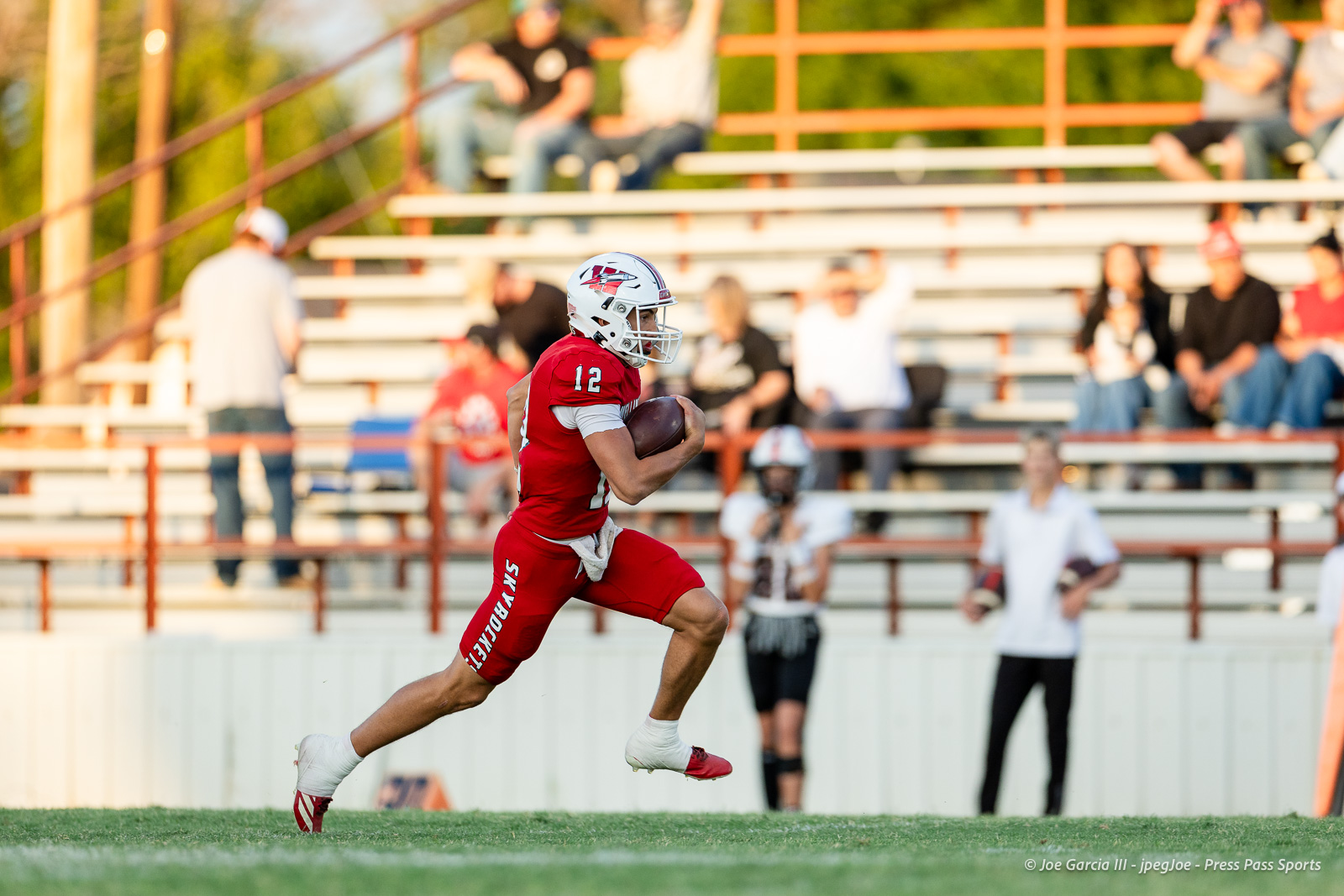 gruver-vs-wellinton-2026-jpegJoe-pps-6 | Press Pass Sports Young football player in red uniform (#12) runs with a football on the field during a game.