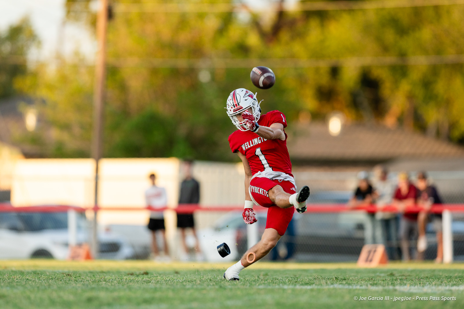 gruver-vs-wellinton-2026-jpegJoe-pps-7 | Press Pass Sports Wellington #1 football player in red jersey leaps to catch a pass on a sunny grass field, spectators in the background.