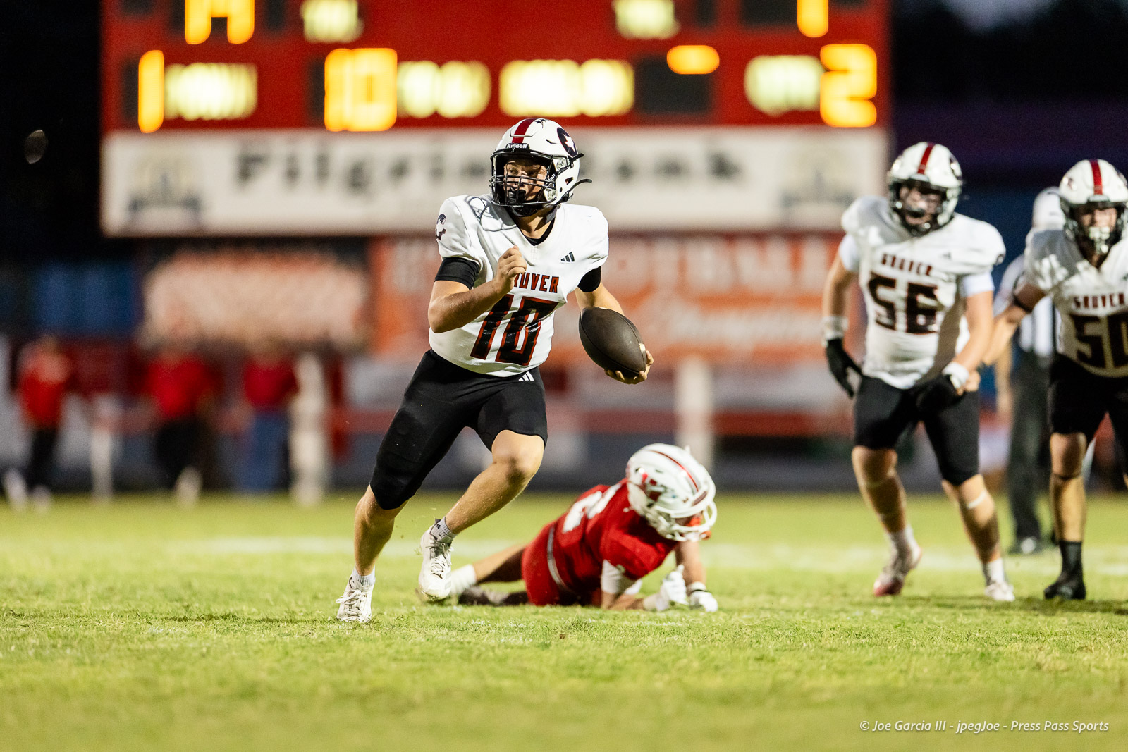 gruver-vs-wellinton-2026-jpegJoe-pps-15 | Press Pass Sports Football quarterback in a white jersey (number 10) sprints with the ball on a grassy field while defenders pursue.