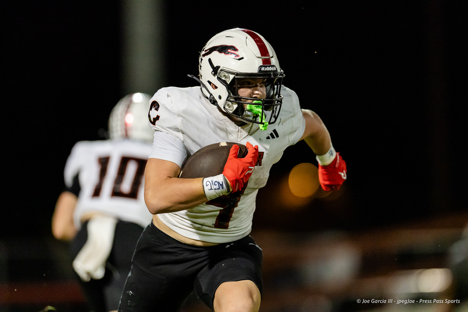 gruver-vs-wellinton-2026-jpegJoe-pps-20 | Press Pass Sports Football player in white jersey #7 carries the ball, rushing forward at night with red gloves and green mouthguard.