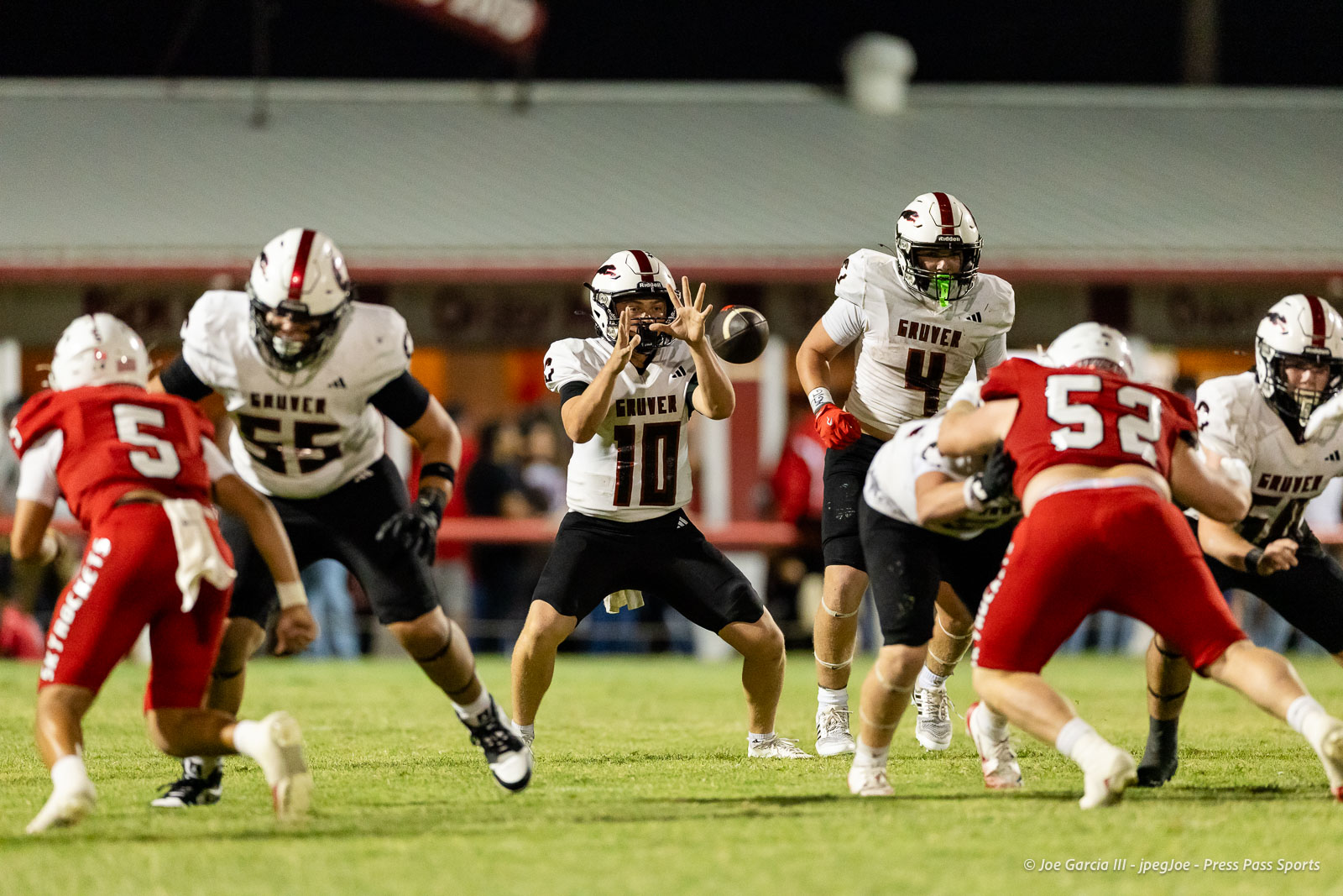 gruver-vs-wellinton-2026-jpegJoe-pps-21 | Press Pass Sports Quarterback #10 in a white Grover jersey throws a pass as teammates block and red defenders rush nearby.
