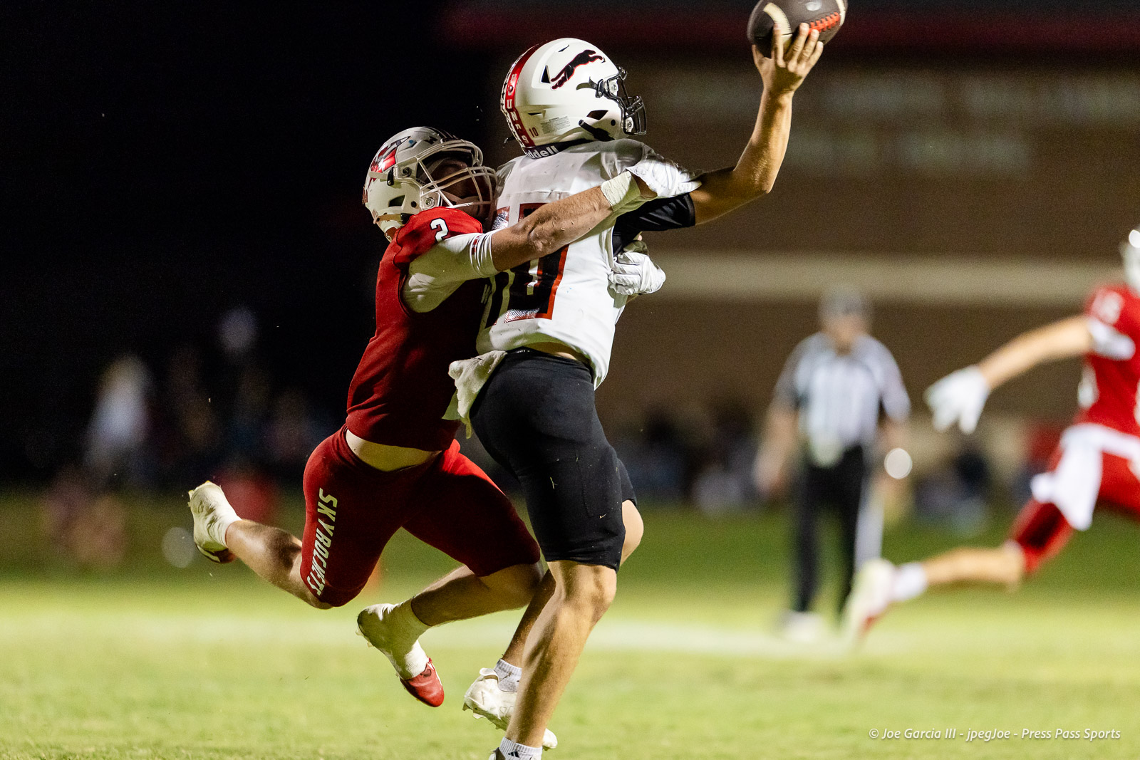 gruver-vs-wellinton-2026-jpegJoe-pps-25 | Press Pass Sports Two football players leap as a defender in red tackles a white-jersey receiver reaching for the ball at night.