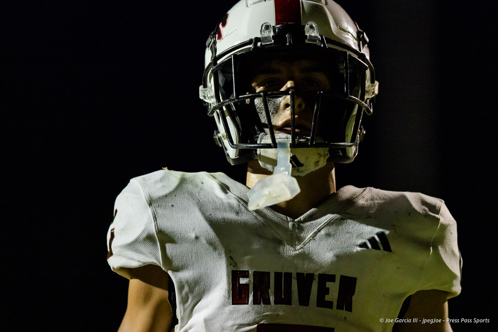gruver-vs-wellinton-2026-jpegJoe-pps-28 | Press Pass Sports Football player in a white jersey and helmet, standing under night lights; the jersey reads'GRUVER' and a mouthguard hangs from the face mask, front-facing shot.