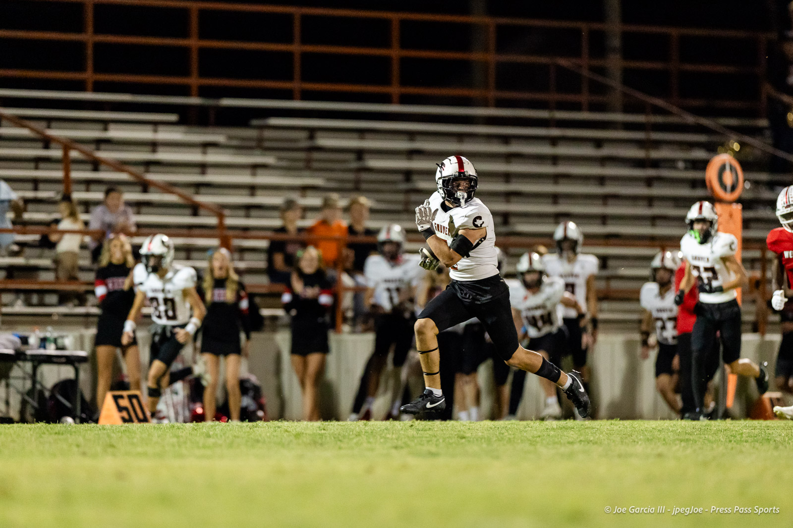 gruver-vs-wellinton-2026-jpegJoe-pps-29 | Press Pass Sports Football player in white jersey running with the ball on a night game, empty bleachers in the background.