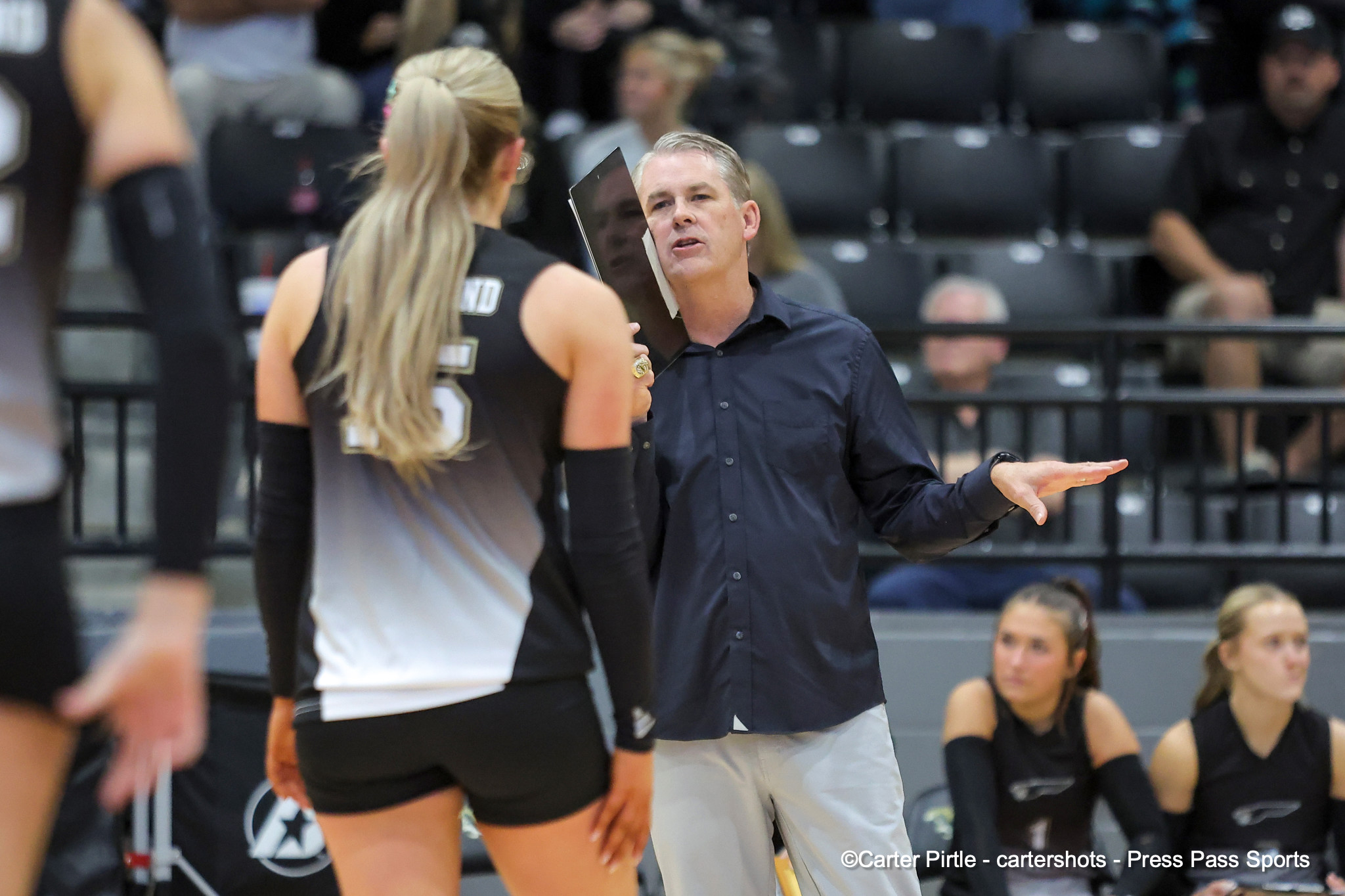 Male coach speaks to volleyball players during a timeout in a gym.