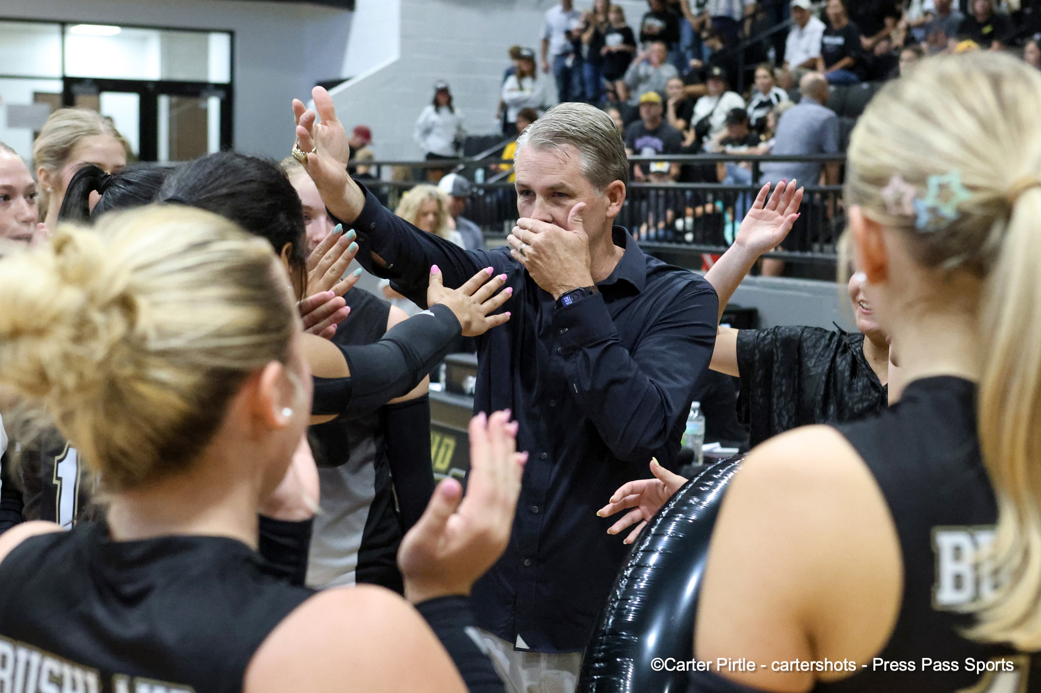 Coach in a dark shirt high-fives a line of fans across a barrier after a game in a gymnasium.