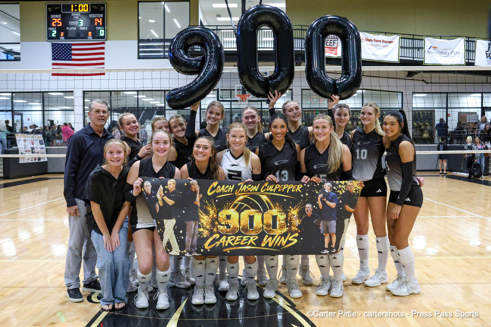 Girls volleyball team posing with coach, holding a banner that reads'Coach Jason Culpepper 900 Career Wins' in a gymnasium.
