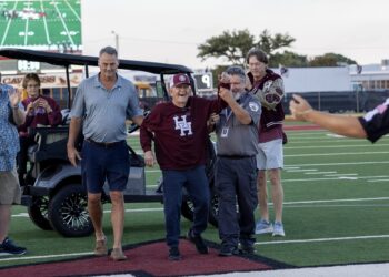 FW9A8451 | Press Pass Sports Group of adults on a football field celebrating near a parked golf cart, with a large scoreboard in the background.