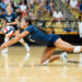 IMG_7725 | Press Pass Sports Female volleyball player in blue dives to save a ball on a polished gym floor with spectators in the stands behind her.