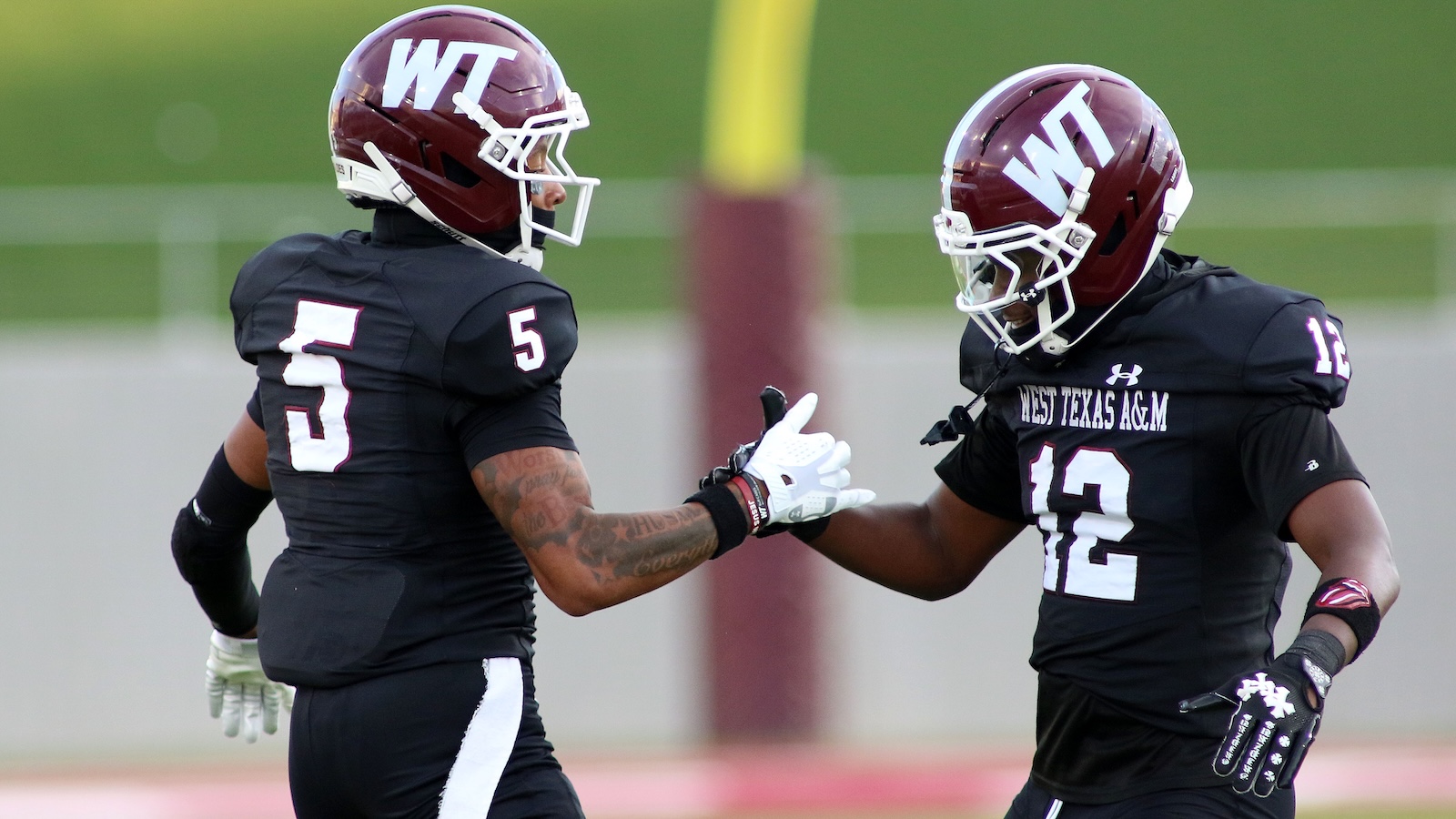 Two football players in black uniforms high-five on a field, helmets with WT logos and numbers 5 and 12 visible.