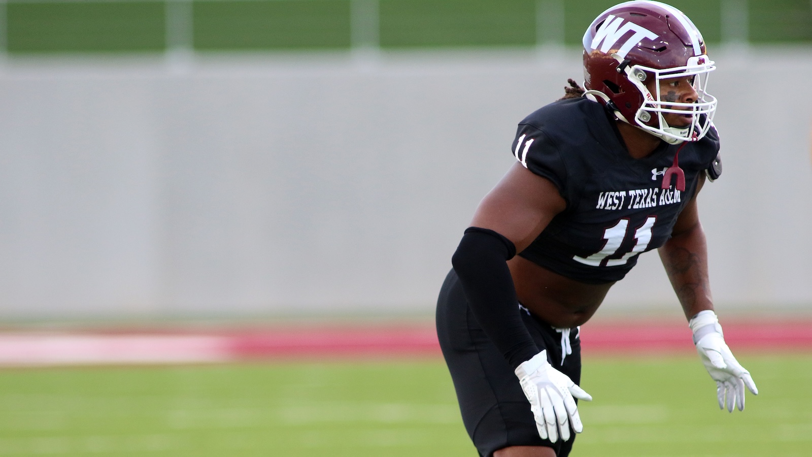 American football player in a black West Texas A&M uniform, number 11, crouching on the field in a game/practice setting.