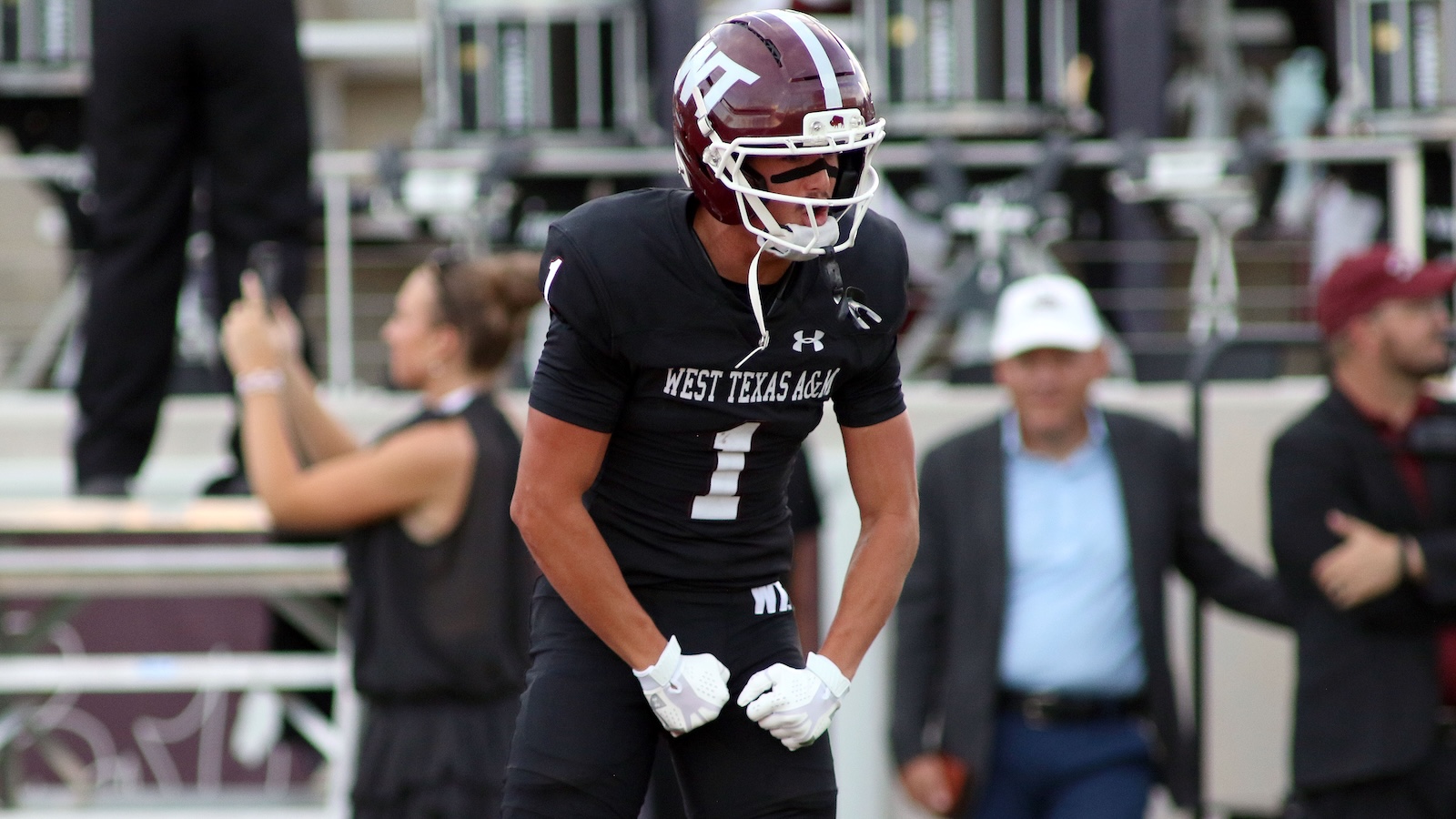 American football player in a black West Texas A&M uniform and helmet, bending forward on the field ready for play (number 1).