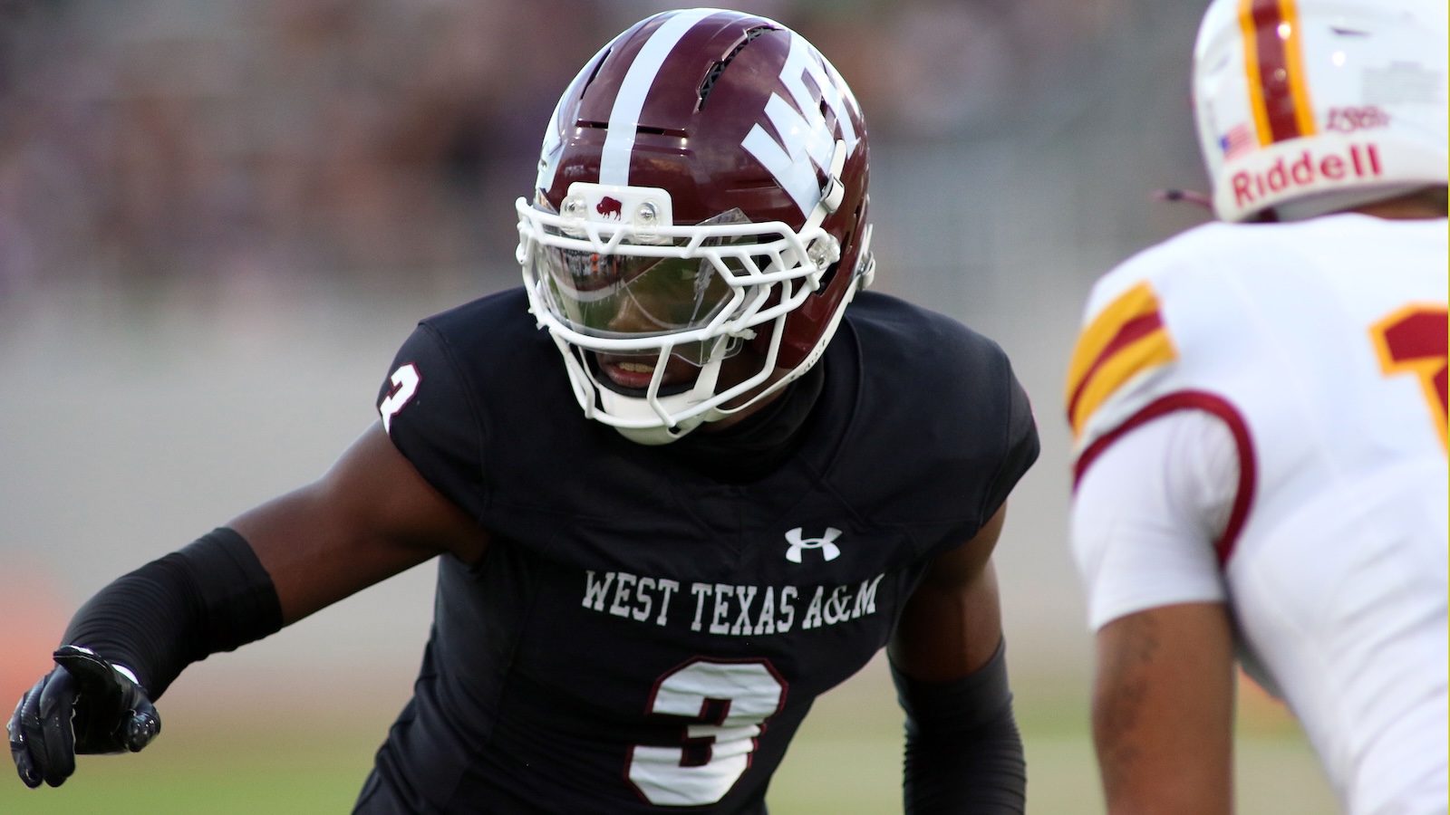 Wide-angle action shot of a West Texas A&M football player in black jersey (#3) pursuing an opponent during a game.