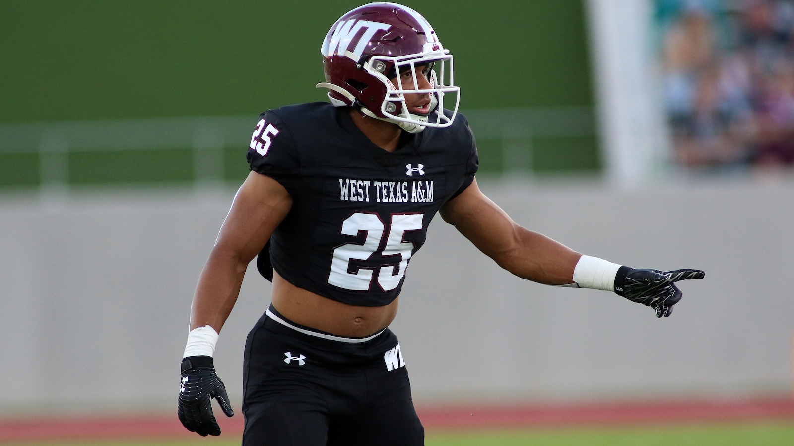 Football player from West Texas A&M in a black uniform, number 25, pointing to the right on the field with a maroon helmet and white face mask